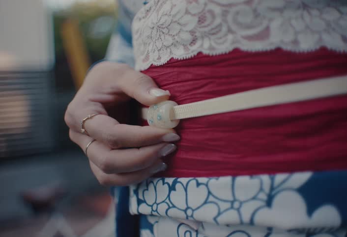 Hand adjusts the red sash of a patterned kimono with lace details