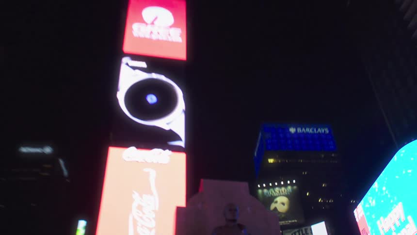 The setting of a busy city at night with a lot of buildings advertisements and a statue