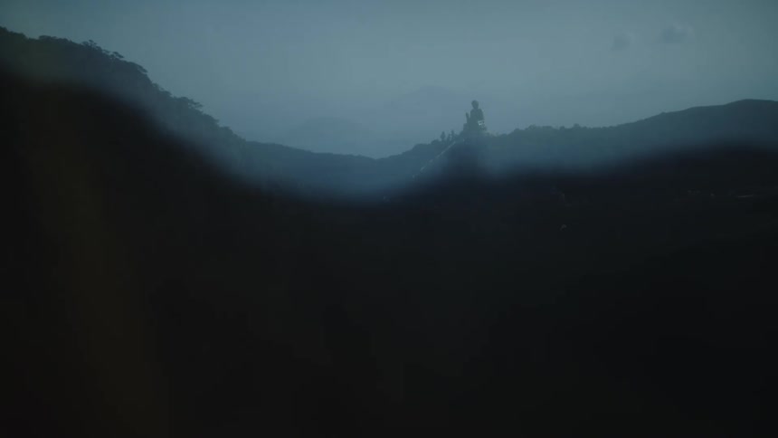 Silhouette of a large statue rises above hills covered in bluish mist