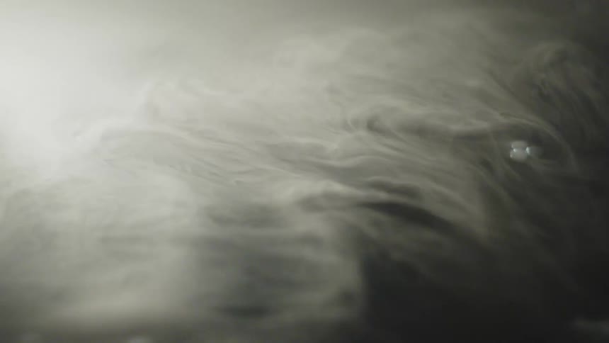 Swirl of smoke or mist spreads gently in a dark environment lit by diffused light