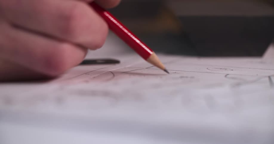A hand holds a pencil and draws a curved line on a piece of paper the pencil is red with a black tip and an eraser on the end