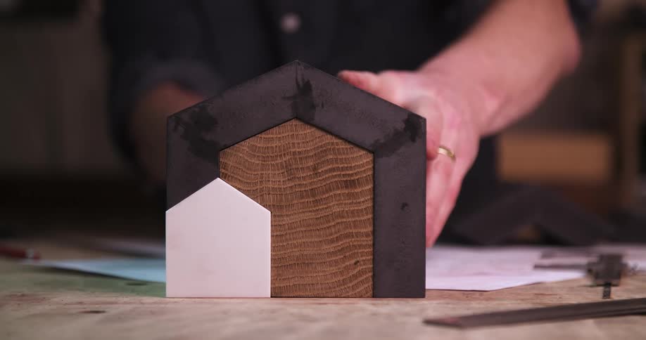 Wooden piece with a geometric structure being adjusted by hands on a workbench