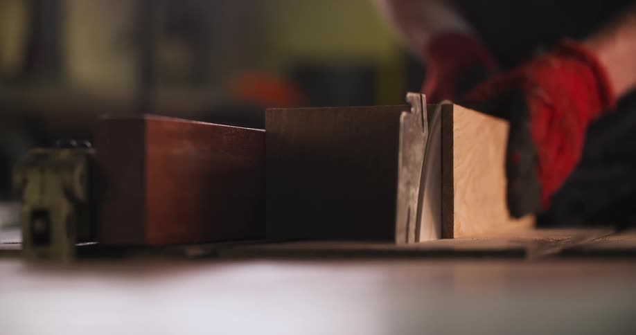 Person wearing red gloves guides circular saw over wood during cut in woodworking setting