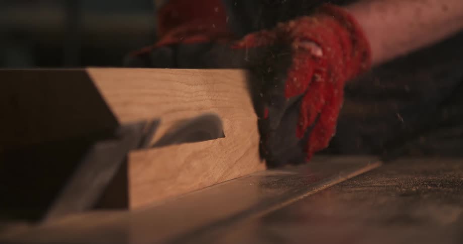 Person wearing red gloves uses hand tool to carve wooden block on workbench