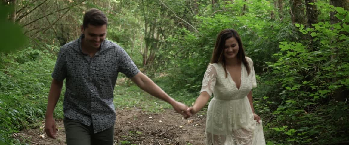 A laughing couple holds hands while walking in the woods