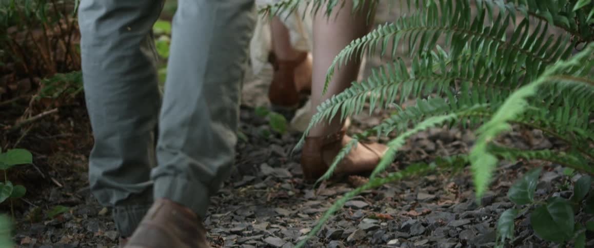 A man and woman are walking on a pebble-strewn path in the woods