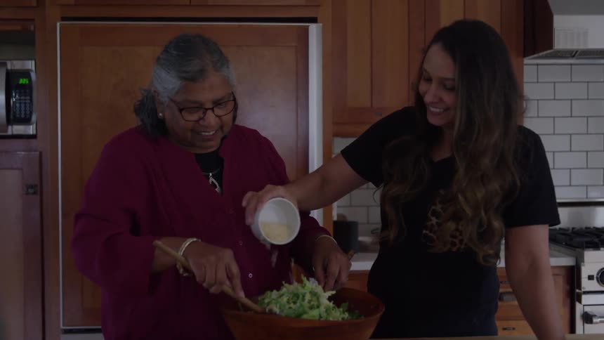 Two women joyfully prepare a salad together in the kitchen