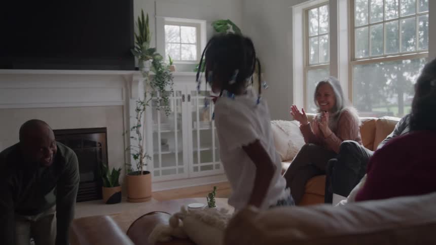 A family is in a living room playing a game and the children are laughing while two older woman are sitting in the couch