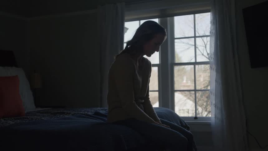 The woman looks sad as she sits on the bed