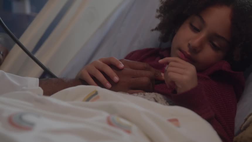 Child lying in a hospital bed holding an adults hand
