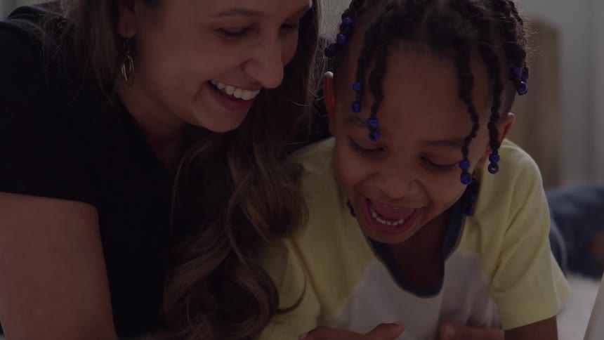 A close view shows a smiling woman with long brown hair next to a young girl with braided hair and blue beads who is laughing joyfully