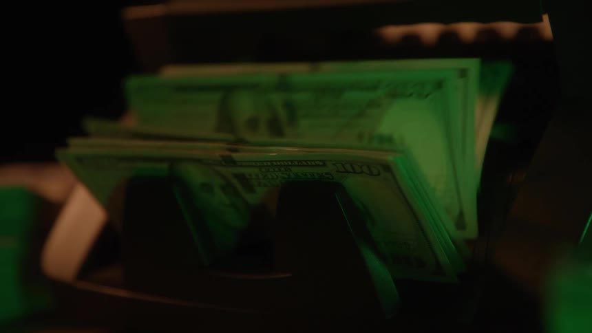 Stacks of money being counted in a machine under green light