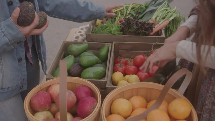 Stalls with fruits vegetables and eggs are arranged at outdoor market with people interacting