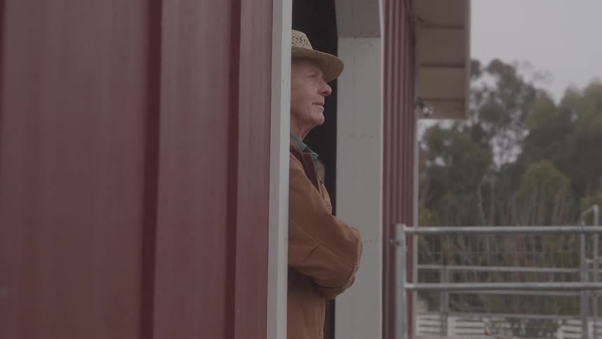 The farmer is standing in the doorway of stable