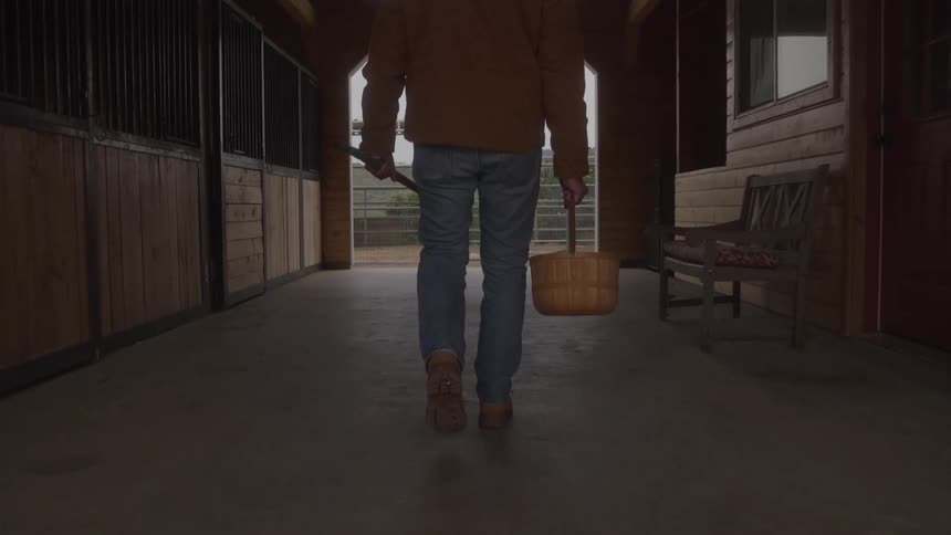 The man carries a wicker basket in the stable