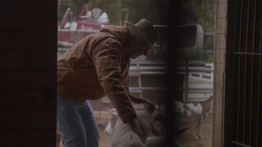 The farmer pets a goat outside the barn