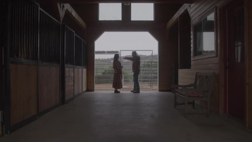 Two people talking inside a stable with a view of the hills in the background