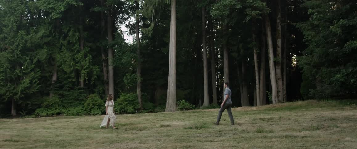 Two people walk down a long field towards each other