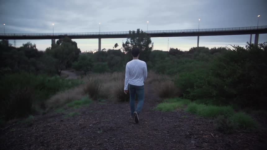 A man walking down a path towards a bridge