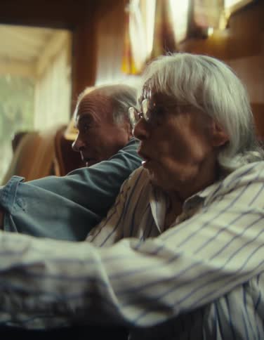 An elderly woman with white hair and glasses looking surprised while watching something off camera