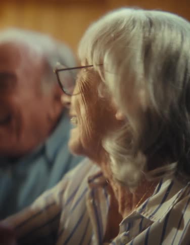 Close up of an elderly man and woman screaming and rejoicing as they watch media content while sitting together in a living room