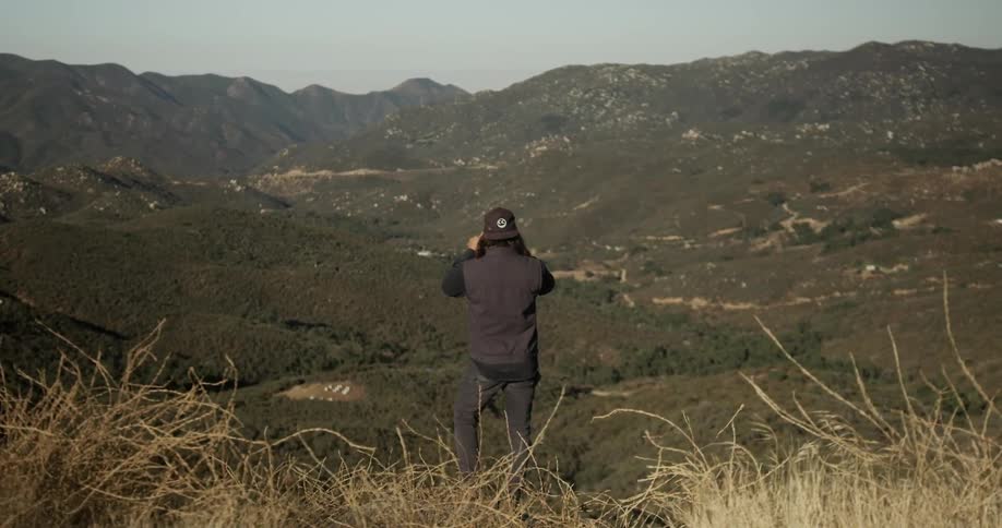 Man standing on top of hillside photographs the view