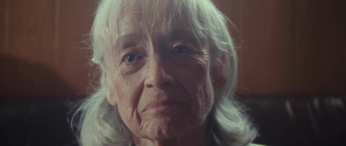 Elderly woman sitting at home tries to frown but starts smiling instead