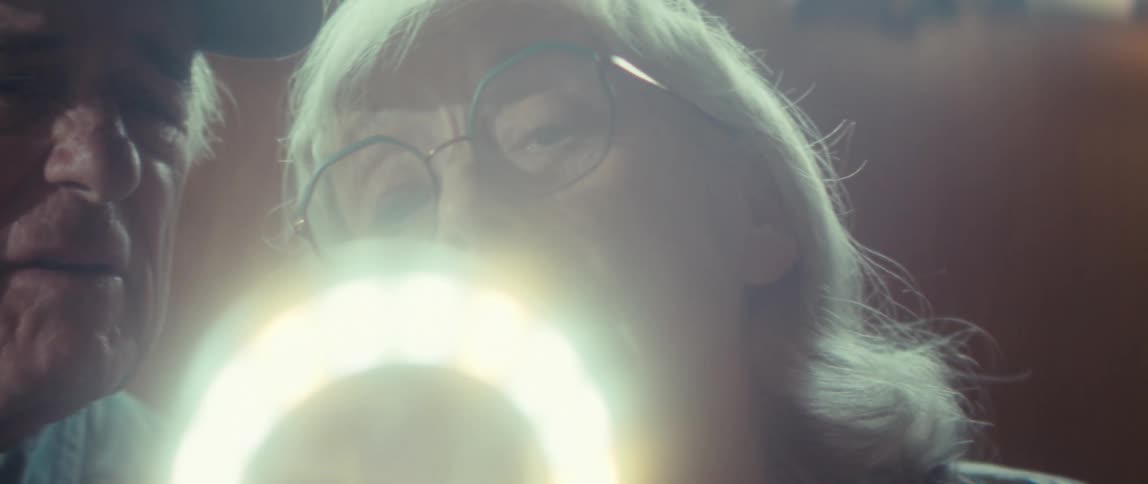 The video is an extreme closeup of a persons hands working on a jigsaw puzzlethe hands are seen picking up and fitting a white puzzle piece with a bright circular light flare into the main image which is out of focus