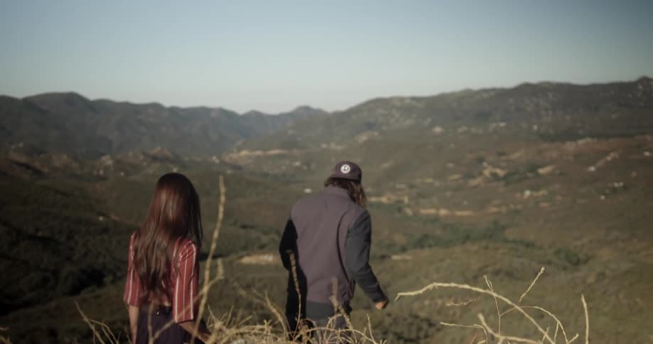 Man and woman walk towards rock high on a hillside