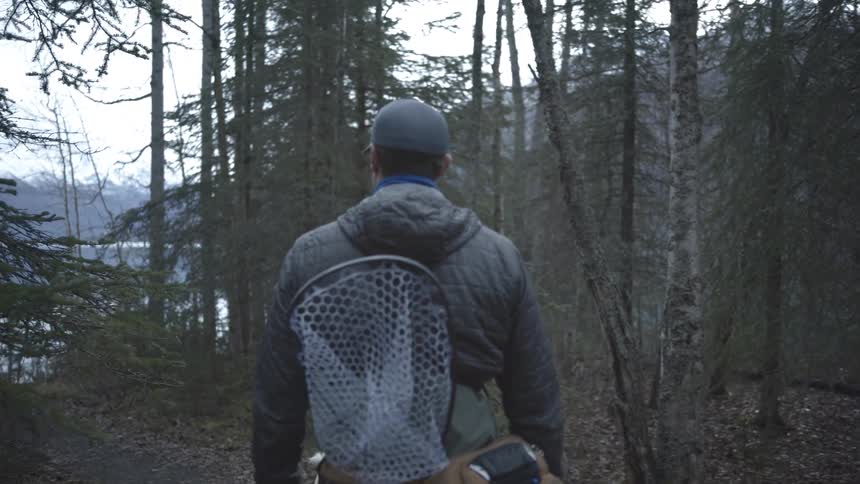 A man carrying fishing equipment walks toward a lake in a forest