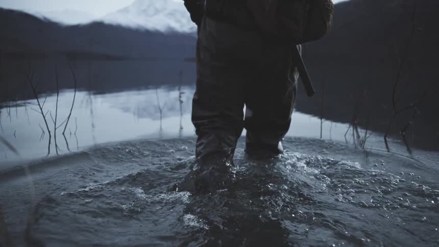 Fisherman walking through shallow waters in a lake surrounded by mountains