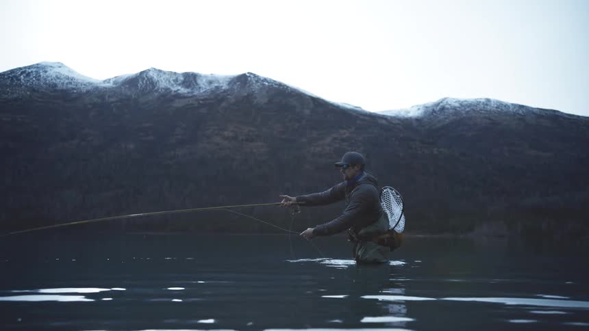 The man swings his fishing pole back in the lake water