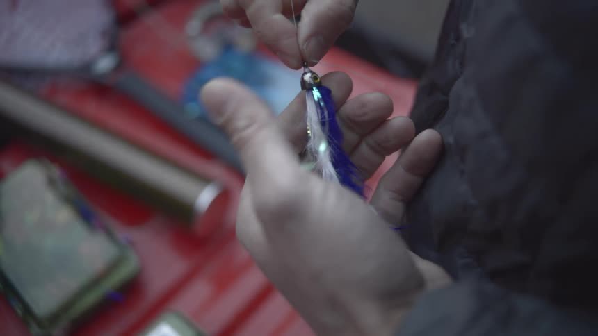 Fisherman in a boat containing fishing items ties a lure onto his line