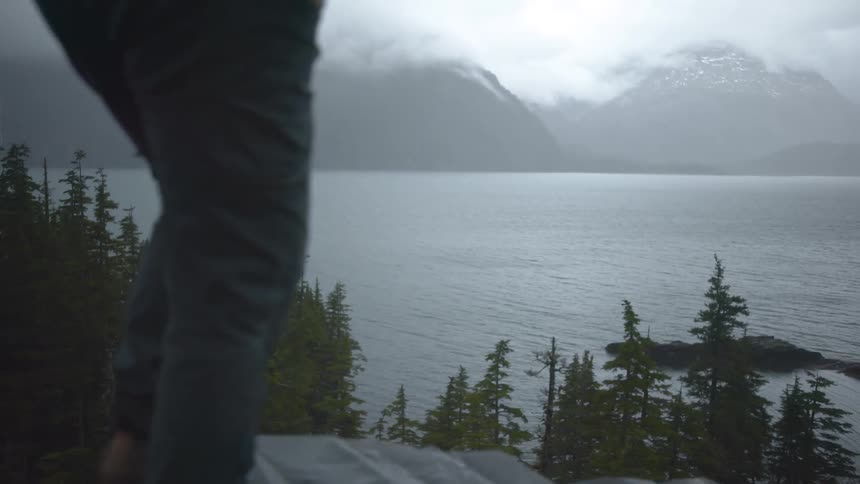 Person climbing on wet rocks with a view of a lake and mountains in the background