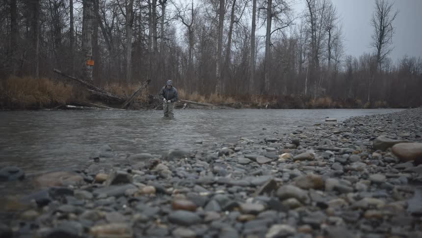 The man stands in the middle of the creek swinging his fishing rod