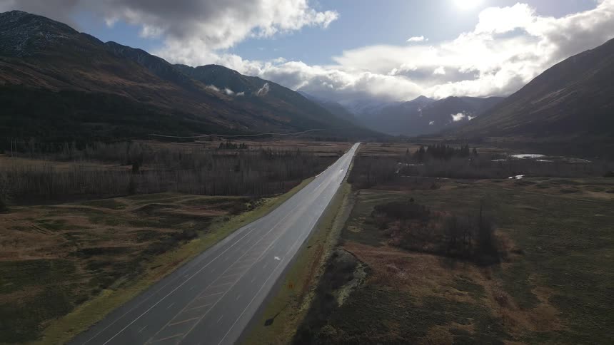 Long straight road stretching through a valley surrounded by mountains under a partly cloudy sky