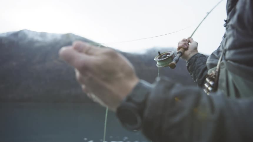 The man casts his fishing pole into the lake water