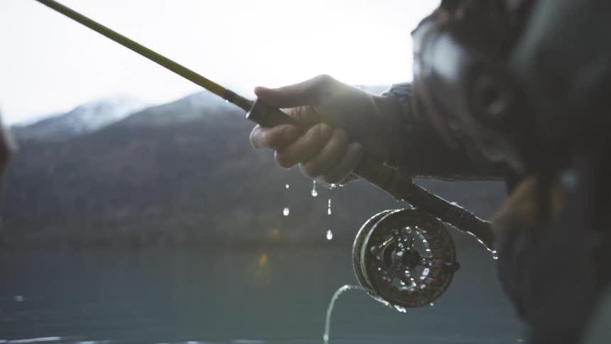 Water flies off of a fishing reel as a fisherman pulls on the line