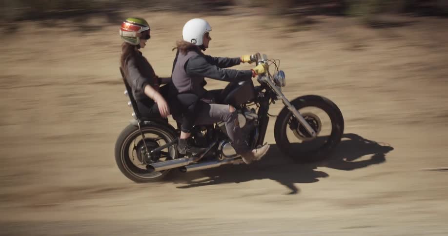 A man and woman are riding on a motorcycle in a desert landscape