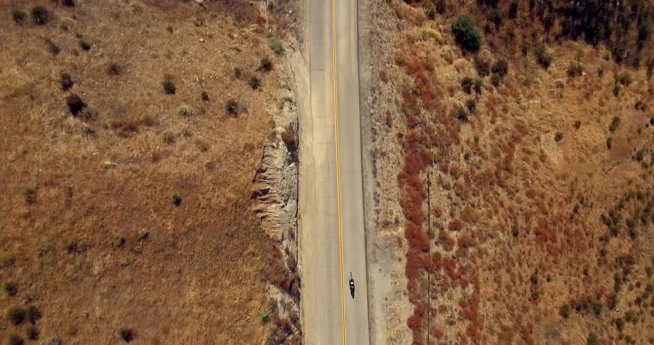 A motorcycle rides down a long barren road
