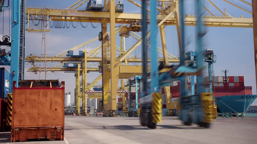 Loading cranes and container movers work to load a container ship at the loading dock on a cloudy day