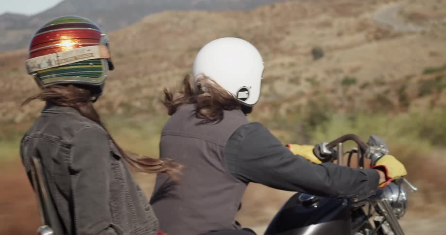 Two people wearing helmets riding a motorcycle