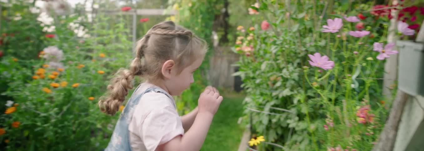 The girl is walking in the garden and smelling the flowers