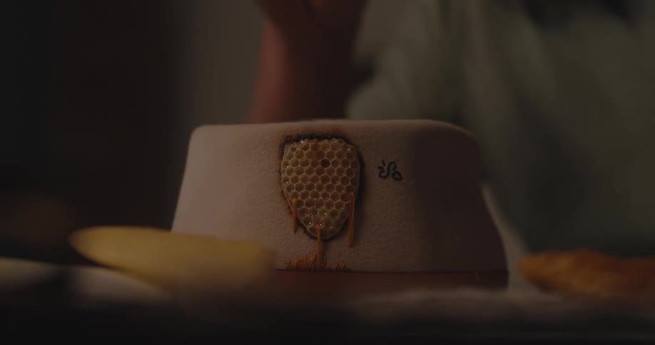 A person sits at the dining table eating with a sun hat placed on top of the table