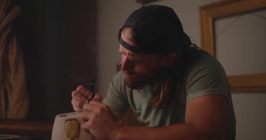 A man is painting a design on a beige hat in a studio