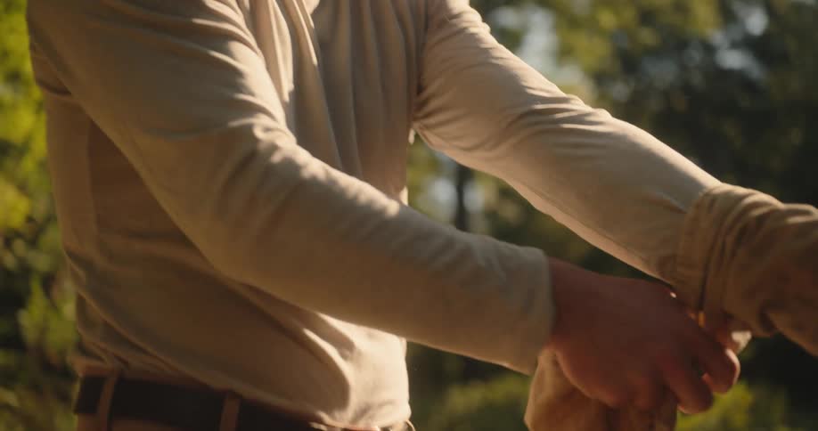 Man puts on protective gloves under sunlight amid vegetation