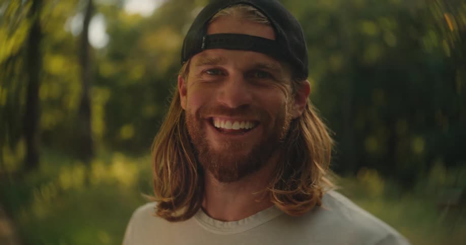 Smiling man wearing a backward cap in a sunlit outdoor setting