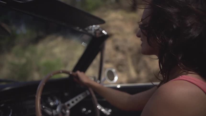 A woman drives a car as the wind blows her hair