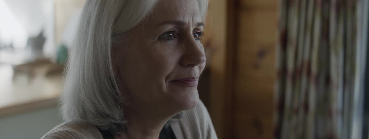 Grayhaired woman smiles softly while observing something around her