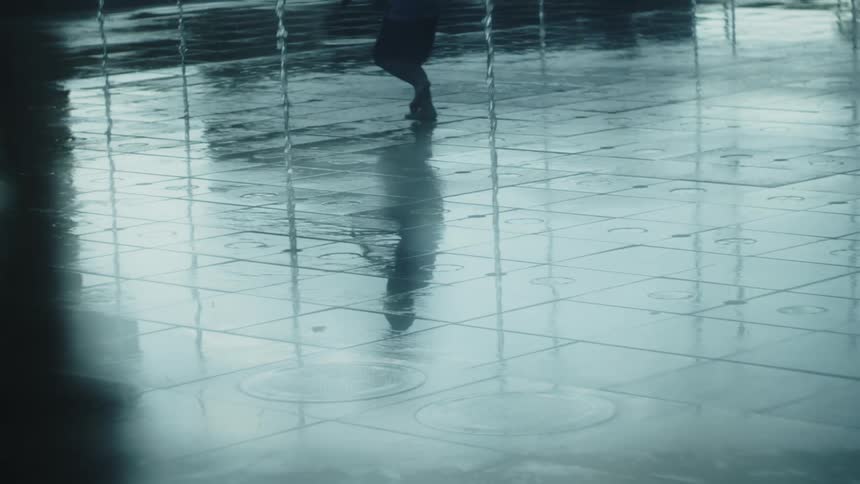 Child runs between water jets reflected on the wet ground